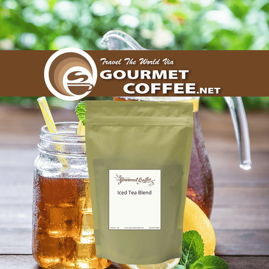 A stand-up pouch of Gourmet Coffee.net Iced Tea Blend stands on a wooden surface in front of a mason jar filled with iced tea and lemon slices, with a pitcher and green foliage blurred in the background.