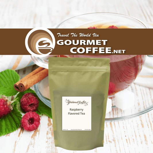 A stand-up pouch of Gourmet Coffee.net Raspberry Flavored Tea placed on a white wood surface with raspberries, cinnamon sticks, green leaves, and a glass of red tea in the background.